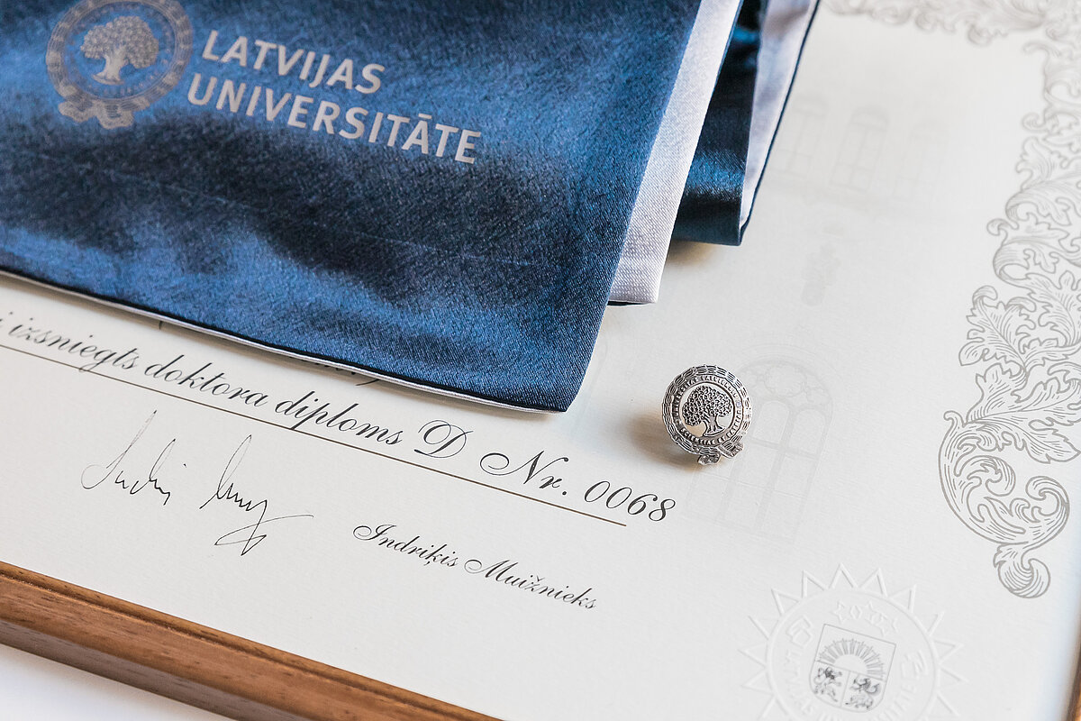 Nozīmīte, šalle un diploms, ko propmocijas ceremonijā saņem doktora grāda ieguvējs
Foto: Toms Grīnbergs, LU Doktora grāda saņēmēja nozīmīte, šalle un diploms